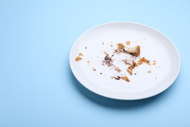 Photo of Dirty plate with crumbs and cream on light blue background, closeup. Space for text