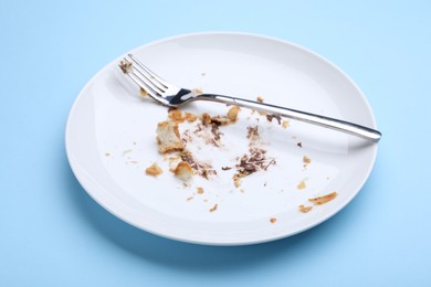 Photo of Dirty plate with crumbs, cream and fork on light blue background, closeup