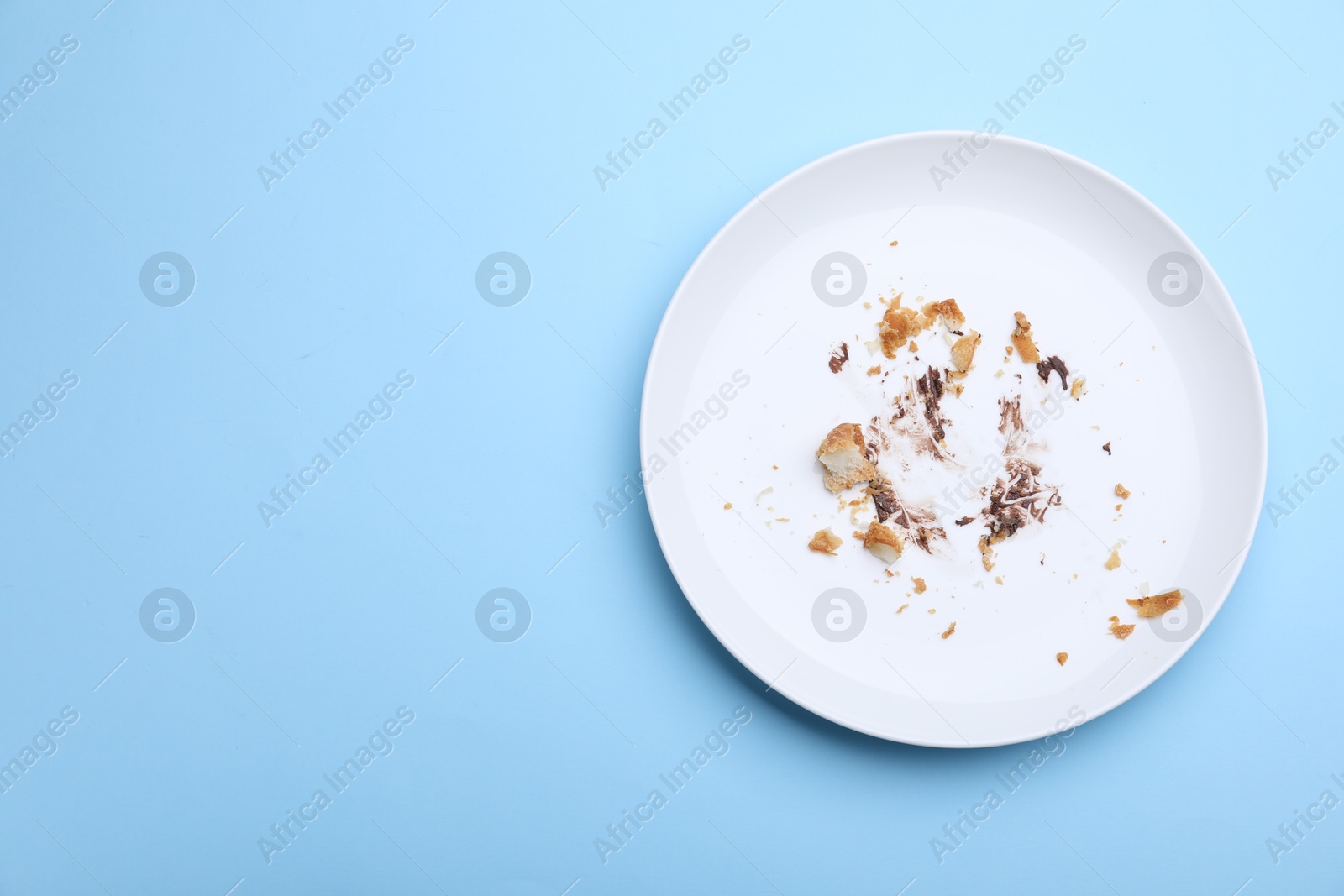 Dirty plate with crumbs and cream on light blue background, top view. Space for text Photo of Dirty plate with crumbs and cream on light blue background, top view. Space for text