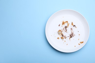 Photo of Dirty plate with crumbs and cream on light blue background, top view. Space for text