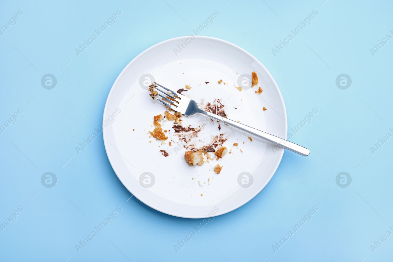 Dirty plate with crumbs, cream and fork on light blue background, top view Photo of Dirty plate with crumbs, cream and fork on light blue background, top view