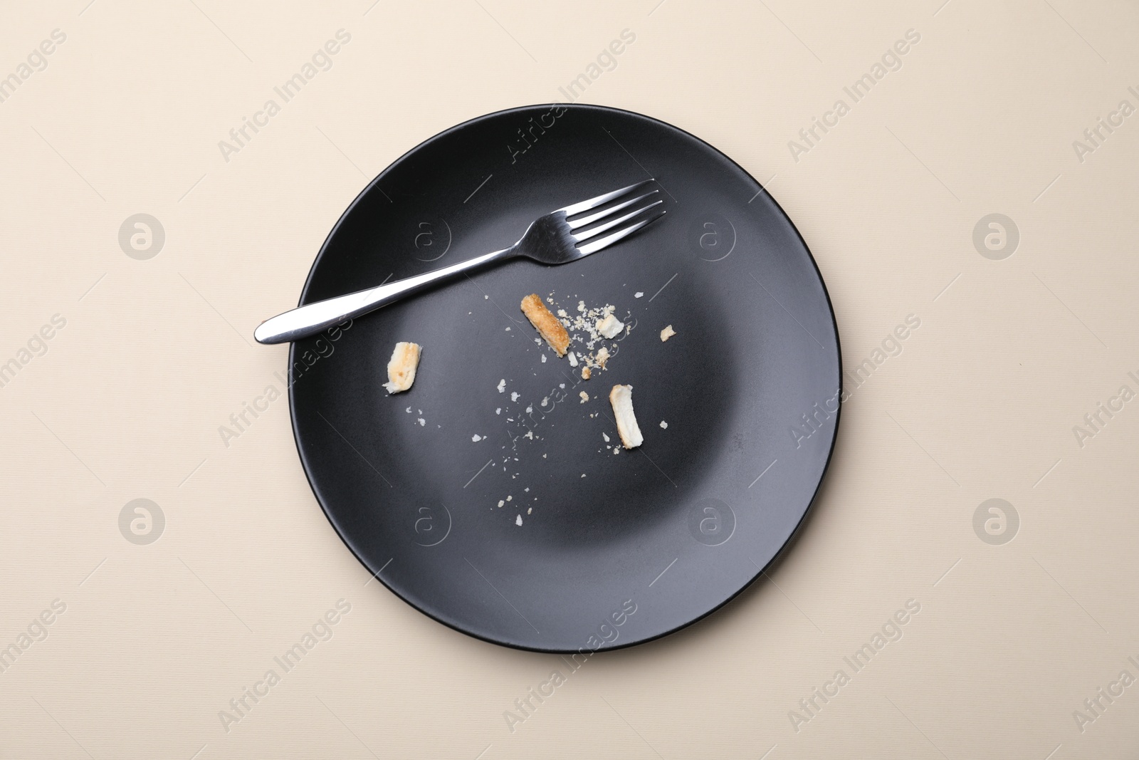 Dirty plate with bread crumbs and fork on beige background, top view Photo of Dirty plate with bread crumbs and fork on beige background, top view