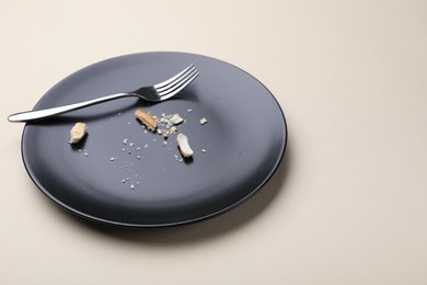 Photo of Dirty plate with bread crumbs and fork on beige background, closeup. Space for text
