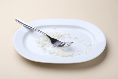 Photo of Dirty plate with rice and fork on beige background, closeup