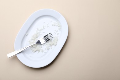 Photo of Dirty plate with rice and fork on beige background, top view. Space for text