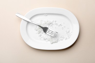 Photo of Dirty plate with rice and fork on beige background, top view