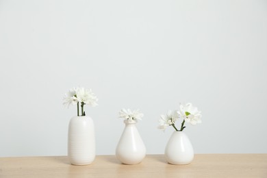 Photo of Beautiful chrysanthemum flowers in vases on wooden table near white wall indoors