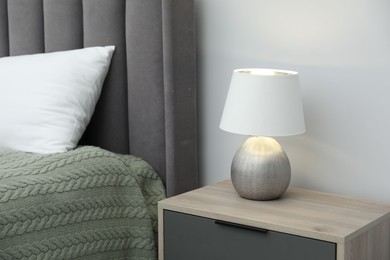 Photo of Lamp on bedside table and bed near white wall indoors