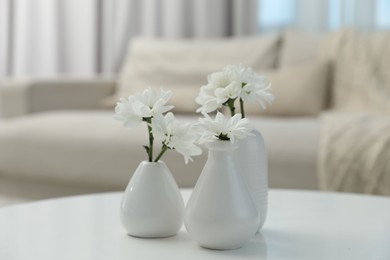 Photo of Beautiful chrysanthemum flowers in vases on white table indoors, closeup
