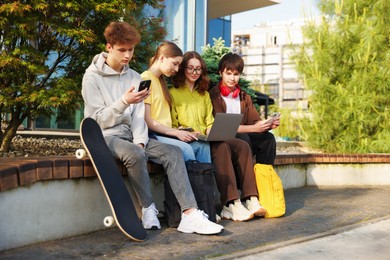 Photo of Teenagers with different devices on bench in park