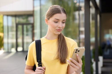 Photo of Teenage girl with smartphone and backpack outdoors
