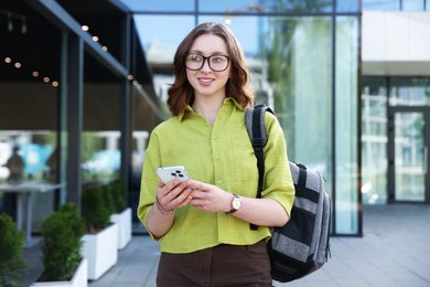 Photo of Teenage girl with smartphone and backpack outdoors