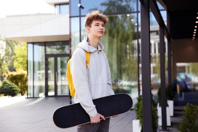 Photo of Teenage boy with skateboard and backpack near building outdoors