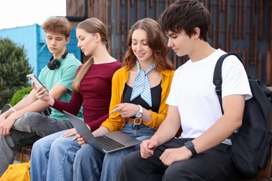 Photo of Teenagers with different devices on bench in park
