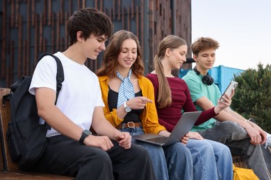 Photo of Teenagers with different devices on bench in park
