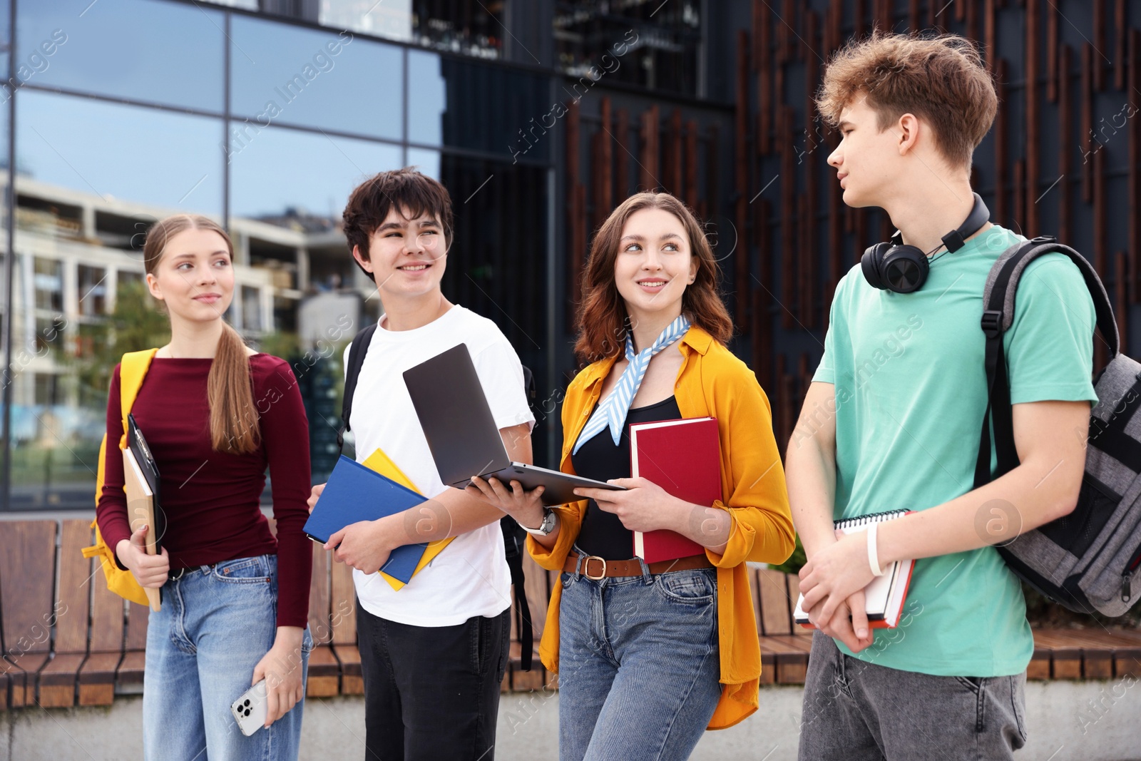 Teenagers with laptop and books near building outdoors Photo of Teenagers with laptop and books near building outdoors