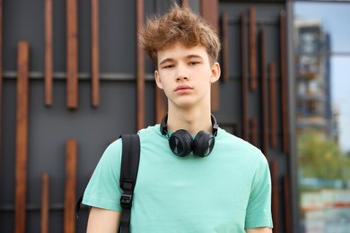 Photo of Teenage boy with headphones and backpack near building outdoors