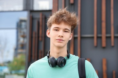 Photo of Teenage boy with headphones and backpack near building outdoors