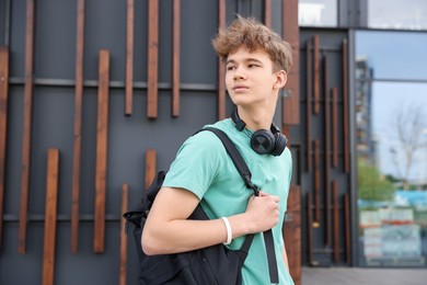 Photo of Teenage boy with headphones and backpack near building outdoors