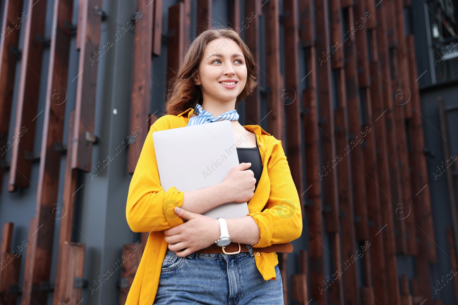 Teenage girl with laptop near building outdoors, low angle view Photo of Teenage girl with laptop near building outdoors, low angle view