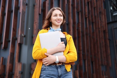 Photo of Teenage girl with laptop near building outdoors, low angle view