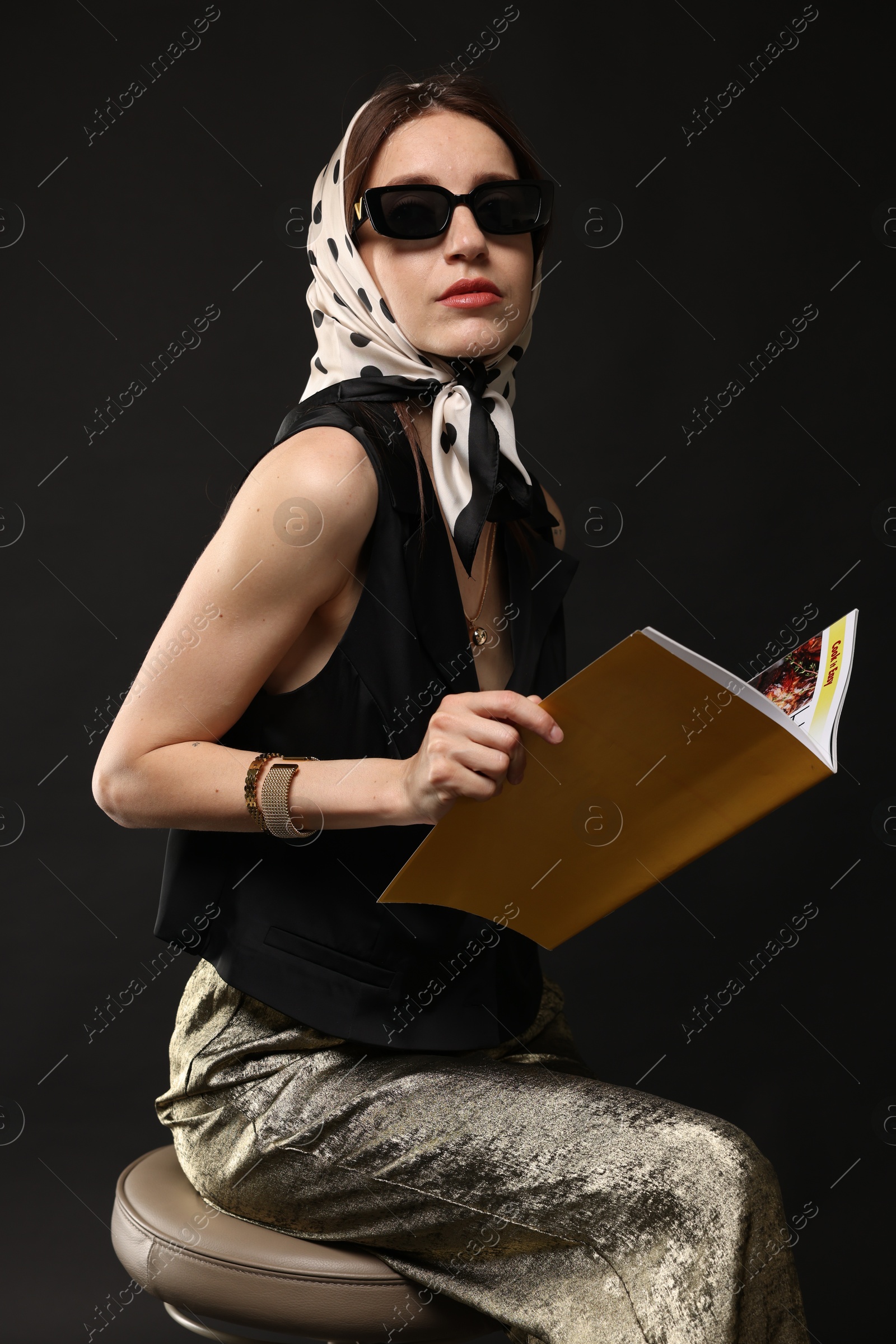 Beautiful woman in stylish outfit with fashion magazine on black background Photo of Beautiful woman in stylish outfit with fashion magazine on black background