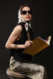 Photo of Beautiful woman in stylish outfit with fashion magazine on black background