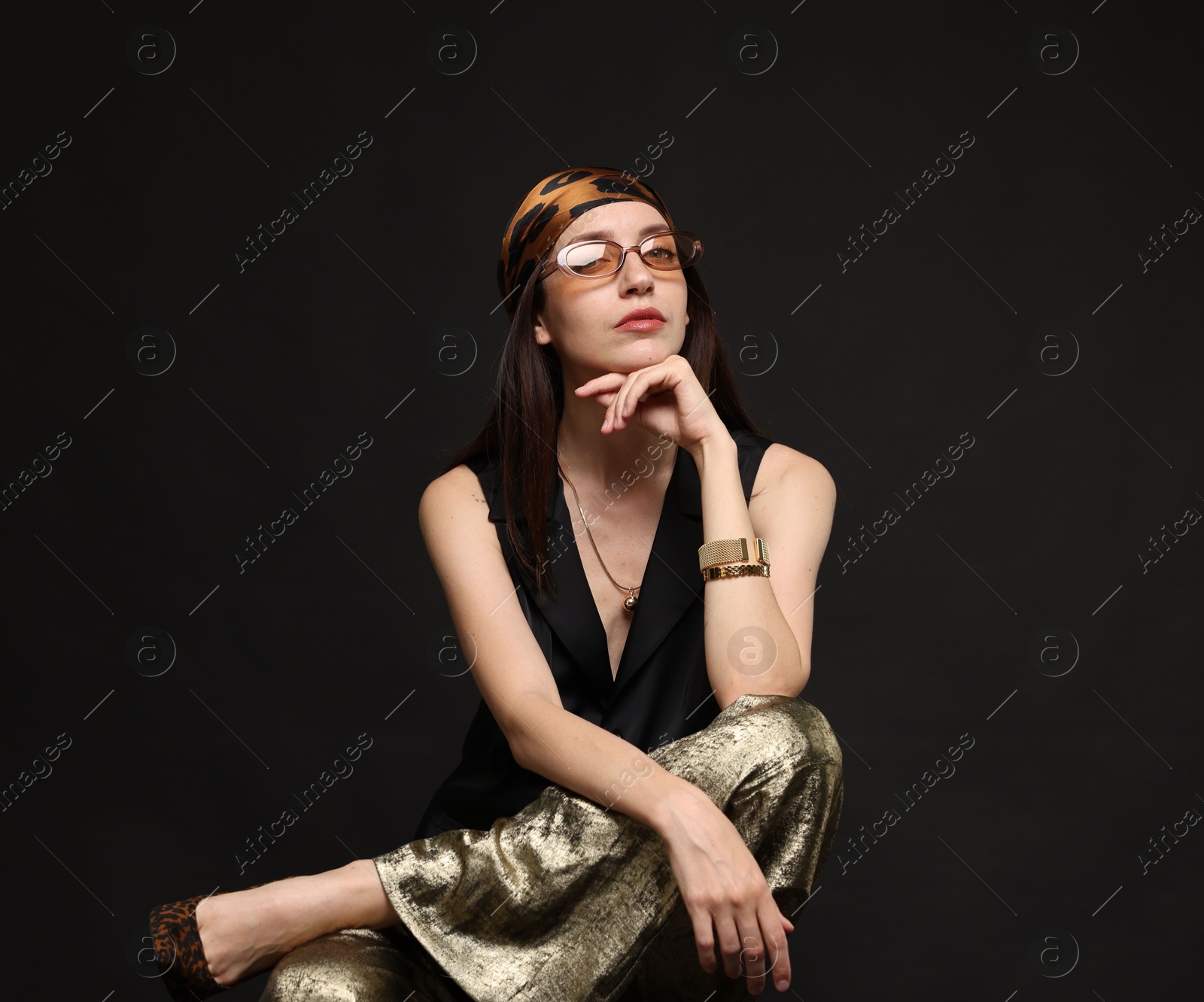 Beautiful woman in stylish outfit sitting on chair against black background Photo of Beautiful woman in stylish outfit sitting on chair against black background