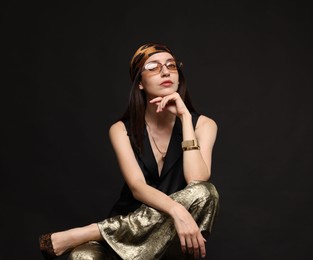 Photo of Beautiful woman in stylish outfit sitting on chair against black background