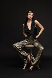 Photo of Beautiful woman in stylish outfit sitting on chair against black background