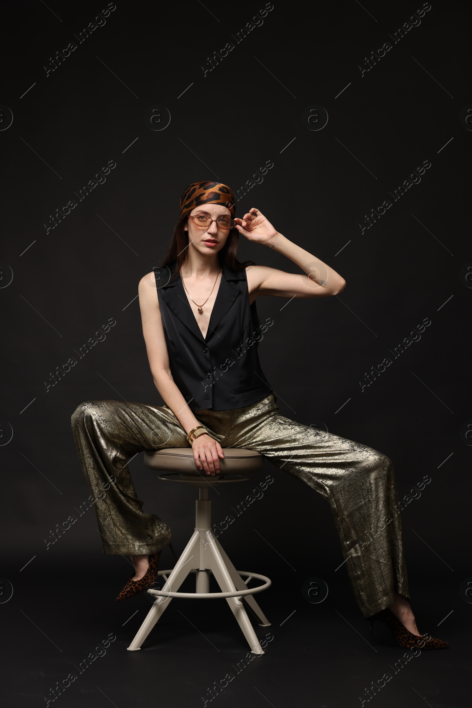 Beautiful woman in stylish outfit sitting on chair against black background Photo of Beautiful woman in stylish outfit sitting on chair against black background