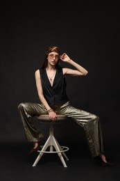 Photo of Beautiful woman in stylish outfit sitting on chair against black background
