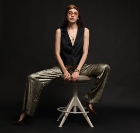 Photo of Beautiful woman in stylish outfit sitting on chair against black background