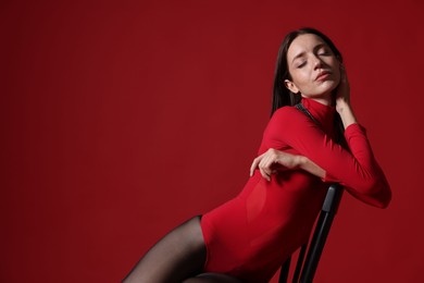 Photo of Beautiful woman in stylish outfit and chair on red background, space for text