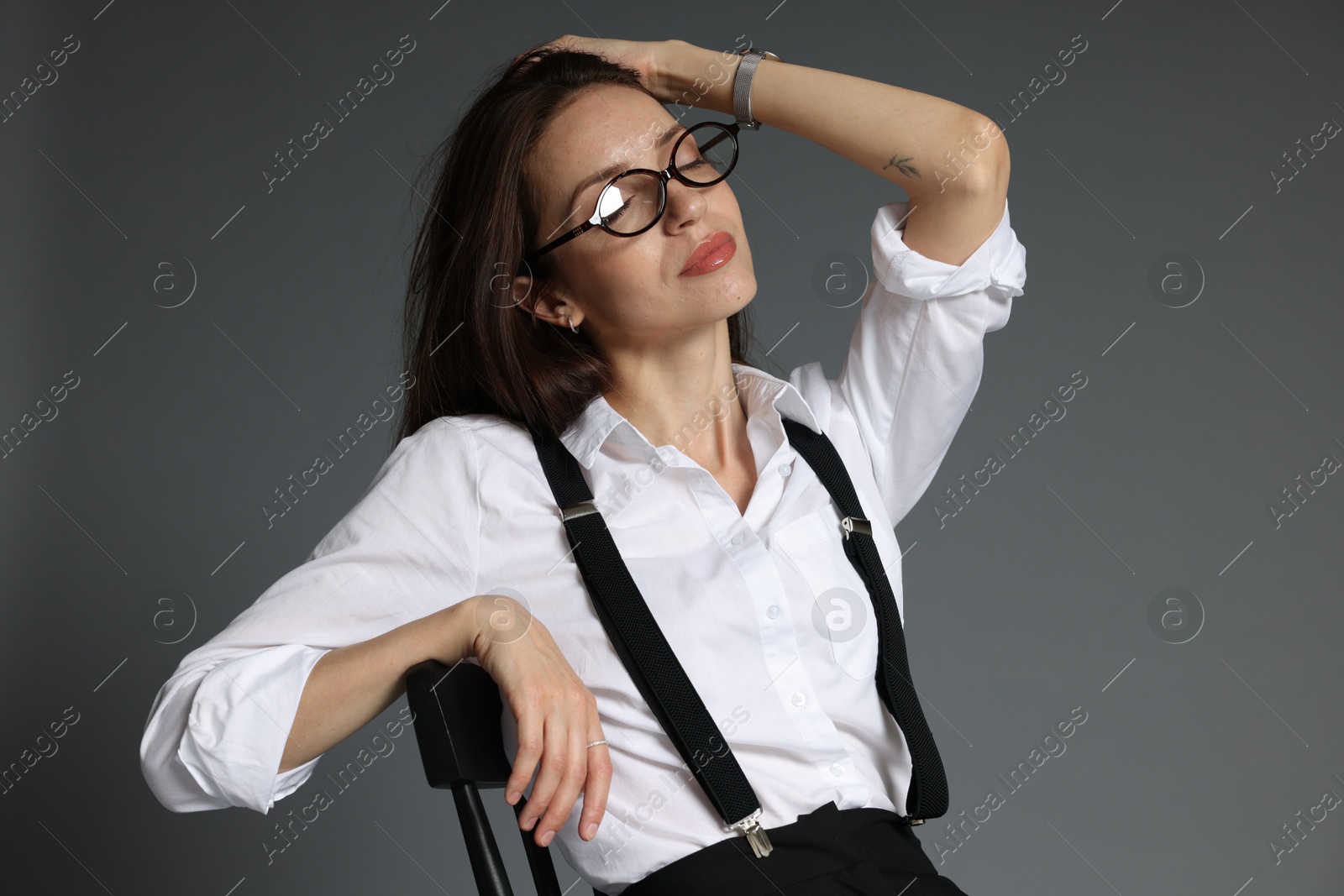 Beautiful woman in stylish outfit sitting on chair against grey background Photo of Beautiful woman in stylish outfit sitting on chair against grey background