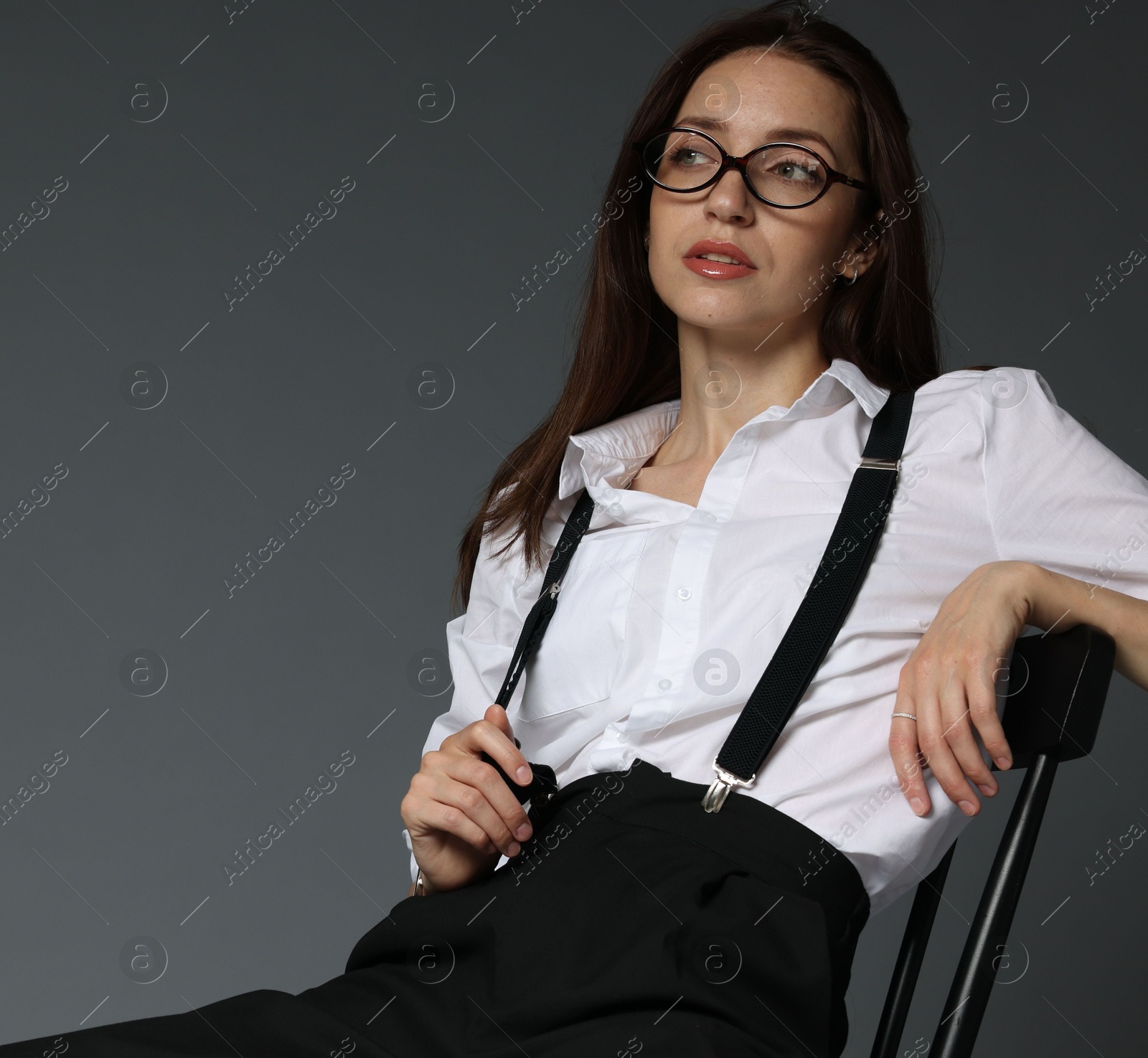 Beautiful woman in stylish outfit sitting on chair against grey background Photo of Beautiful woman in stylish outfit sitting on chair against grey background