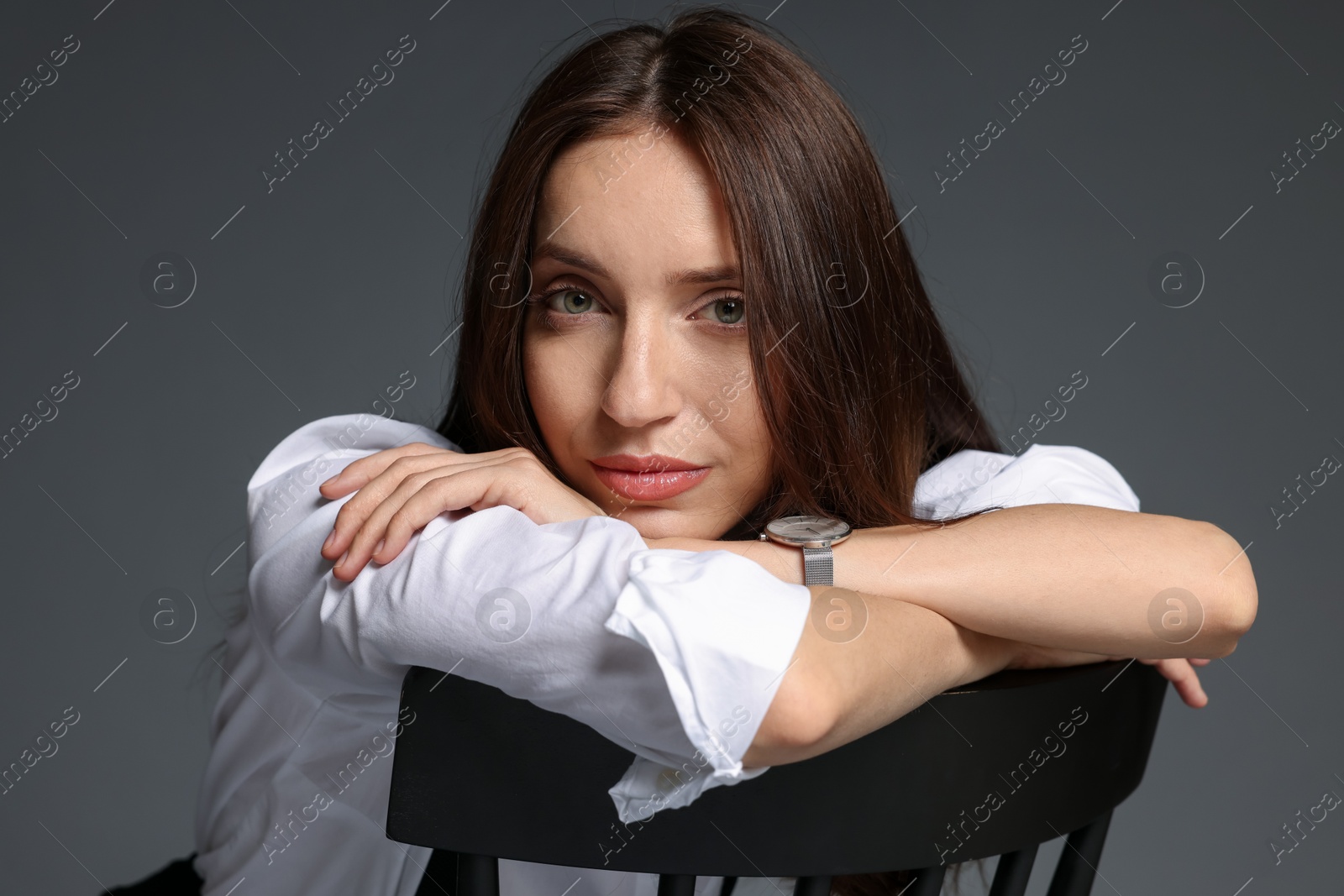 Beautiful woman in stylish outfit sitting on chair against grey background Photo of Beautiful woman in stylish outfit sitting on chair against grey background