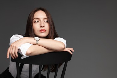 Photo of Beautiful woman in stylish outfit sitting on chair against grey background, space for text