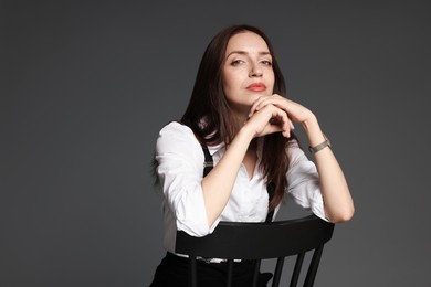 Photo of Beautiful woman in stylish outfit sitting on chair against grey background, space for text