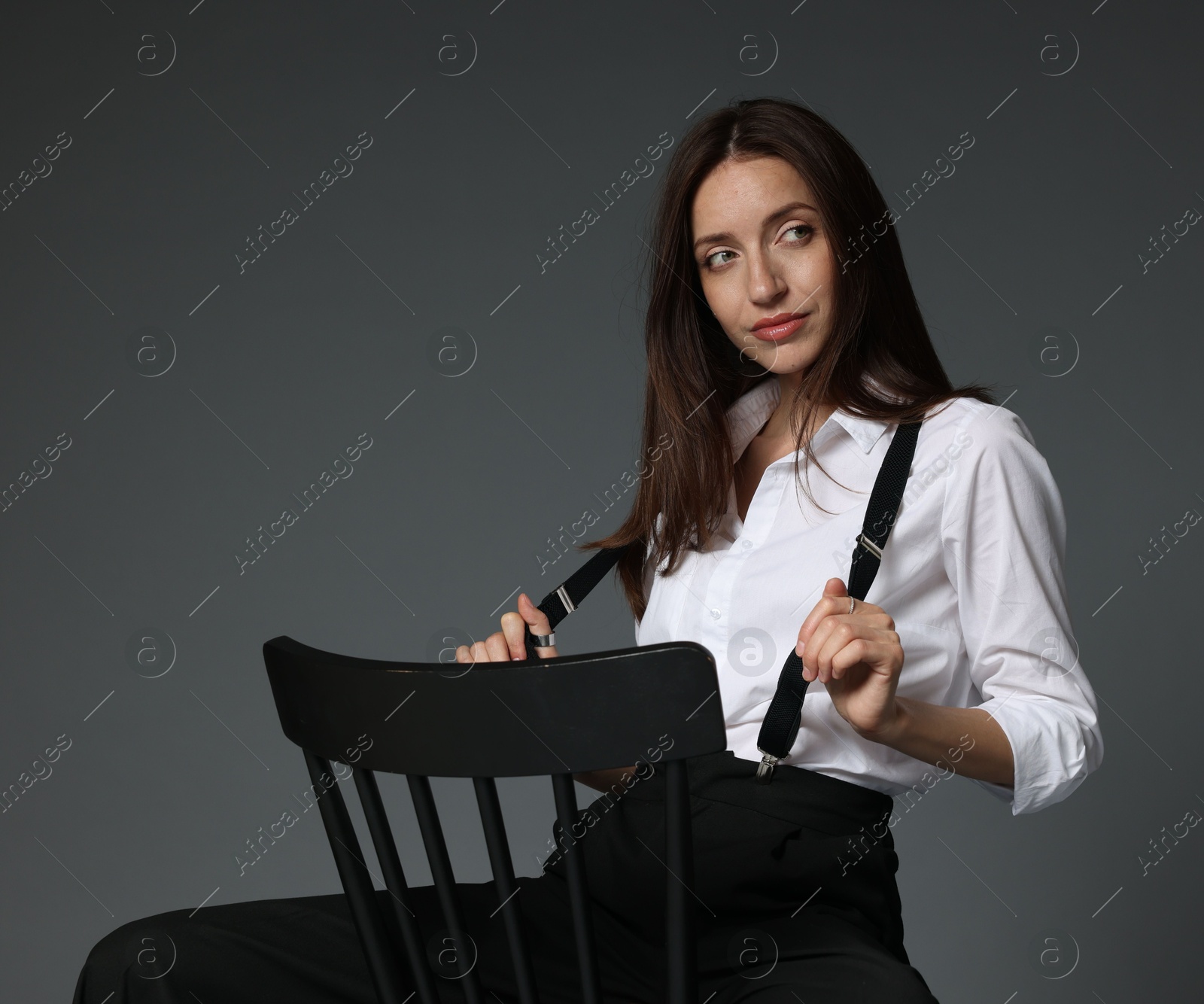 Beautiful woman in stylish outfit sitting on chair against grey background Photo of Beautiful woman in stylish outfit sitting on chair against grey background