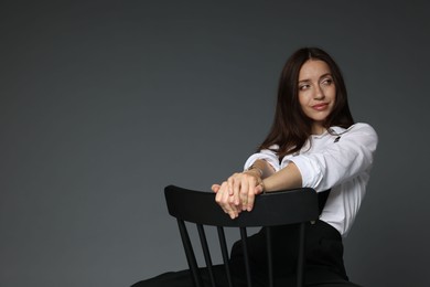 Photo of Beautiful woman in stylish outfit sitting on chair against grey background, space for text