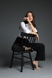 Photo of Beautiful woman in stylish outfit sitting on chair against grey background