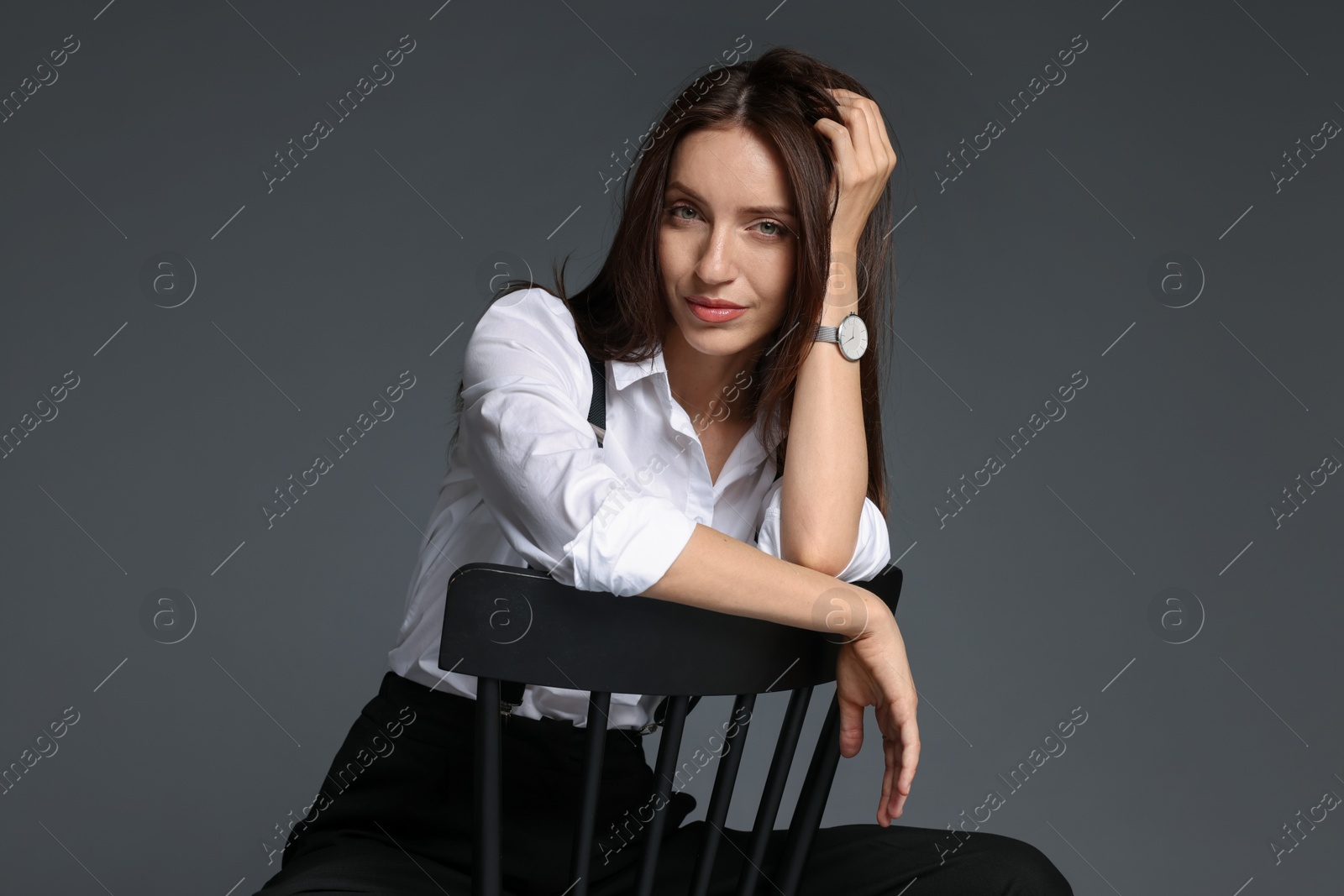 Beautiful woman in stylish outfit sitting on chair against grey background Photo of Beautiful woman in stylish outfit sitting on chair against grey background