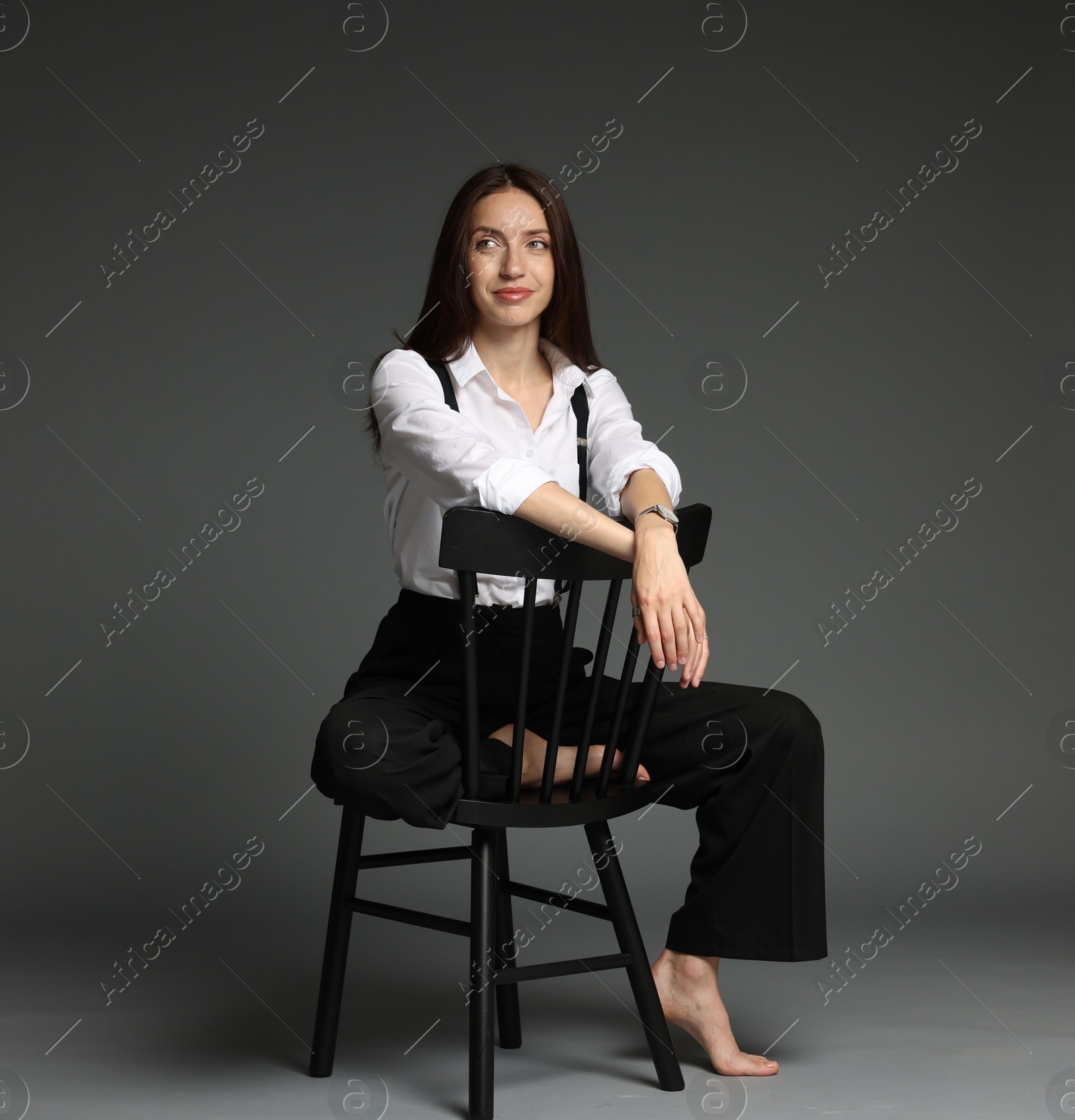 Beautiful woman in stylish outfit sitting on chair against grey background Photo of Beautiful woman in stylish outfit sitting on chair against grey background
