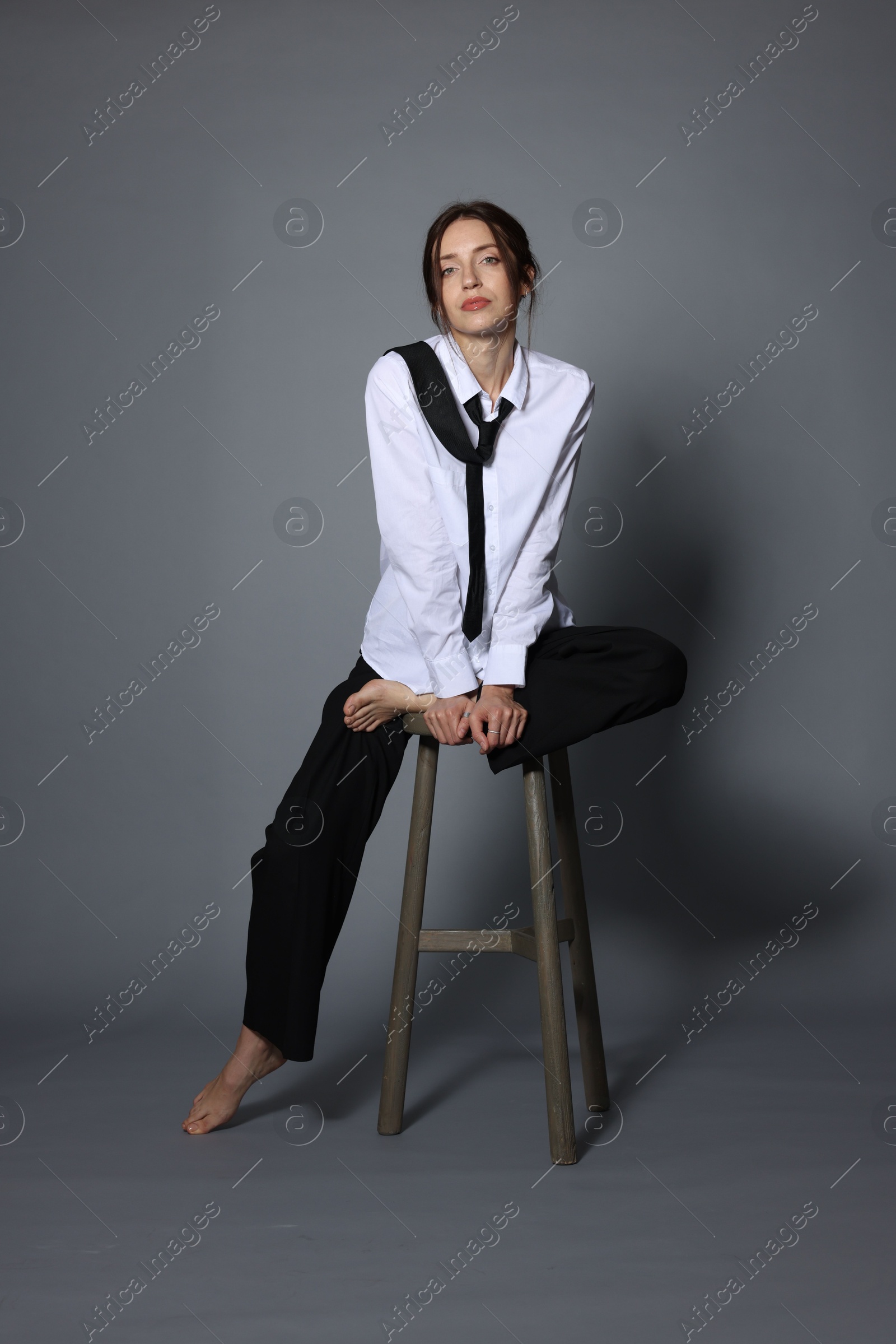 Beautiful woman in stylish outfit sitting on chair against light grey background Photo of Beautiful woman in stylish outfit sitting on chair against light grey background