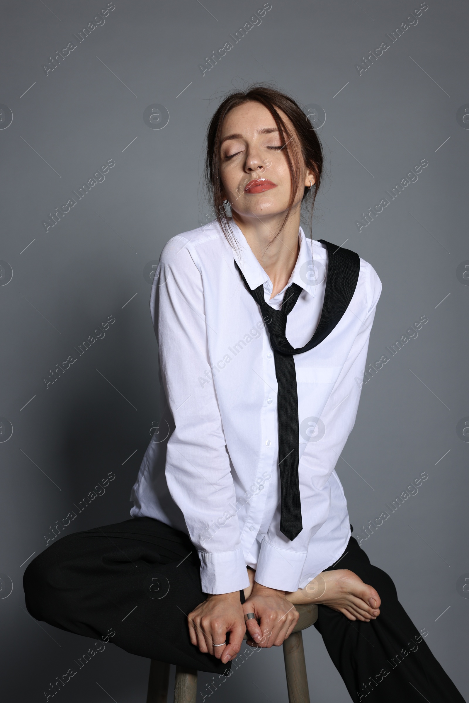 Beautiful woman in stylish outfit sitting on chair against light grey background Photo of Beautiful woman in stylish outfit sitting on chair against light grey background