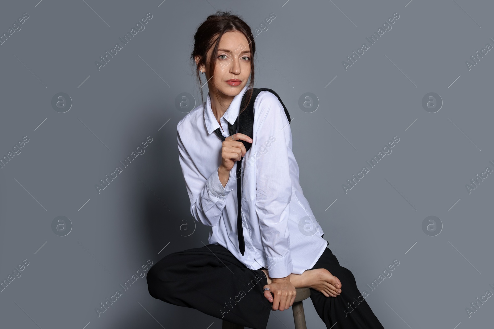 Beautiful woman in stylish outfit sitting on chair against light grey background Photo of Beautiful woman in stylish outfit sitting on chair against light grey background