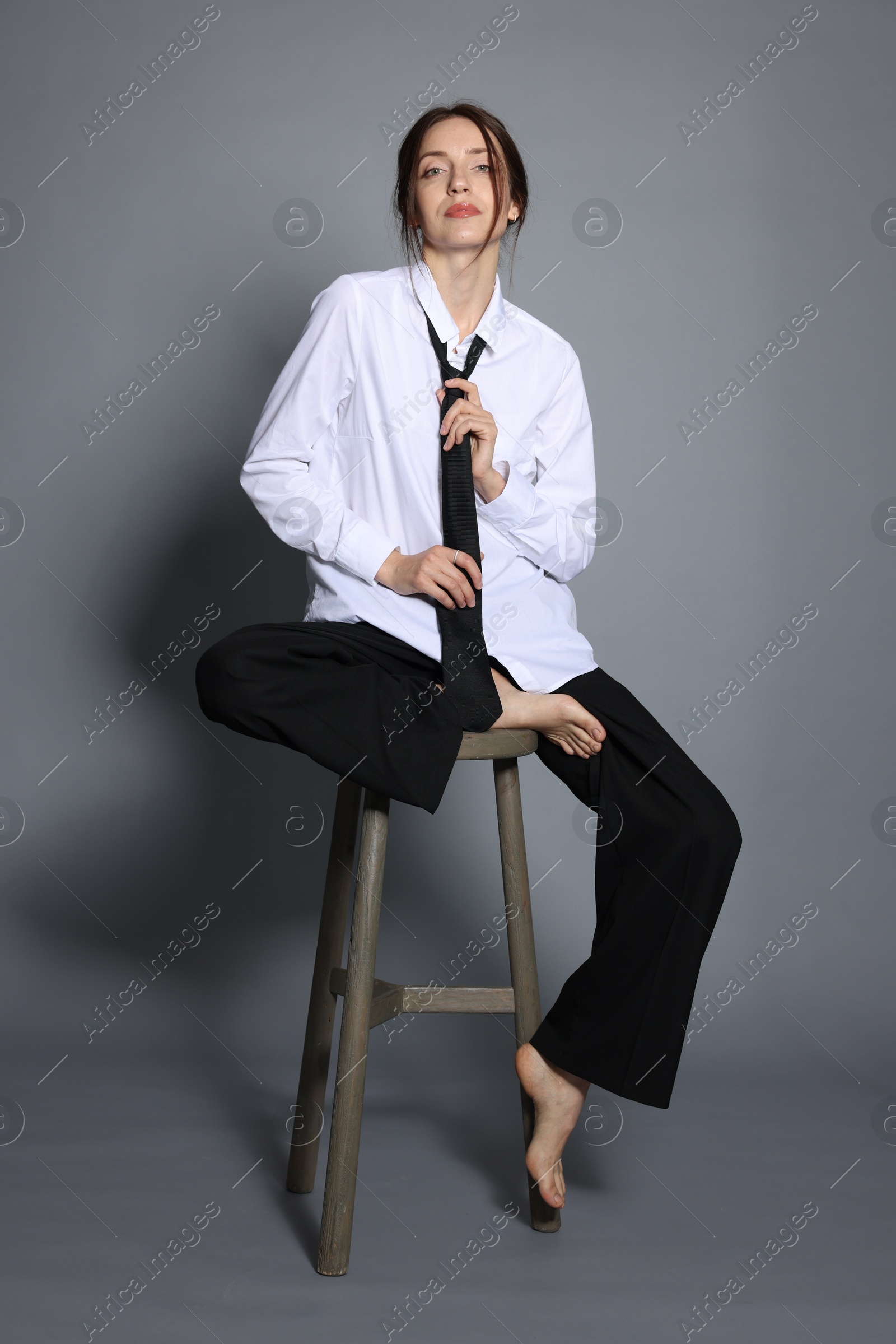 Beautiful woman in stylish outfit sitting on chair against light grey background Photo of Beautiful woman in stylish outfit sitting on chair against light grey background