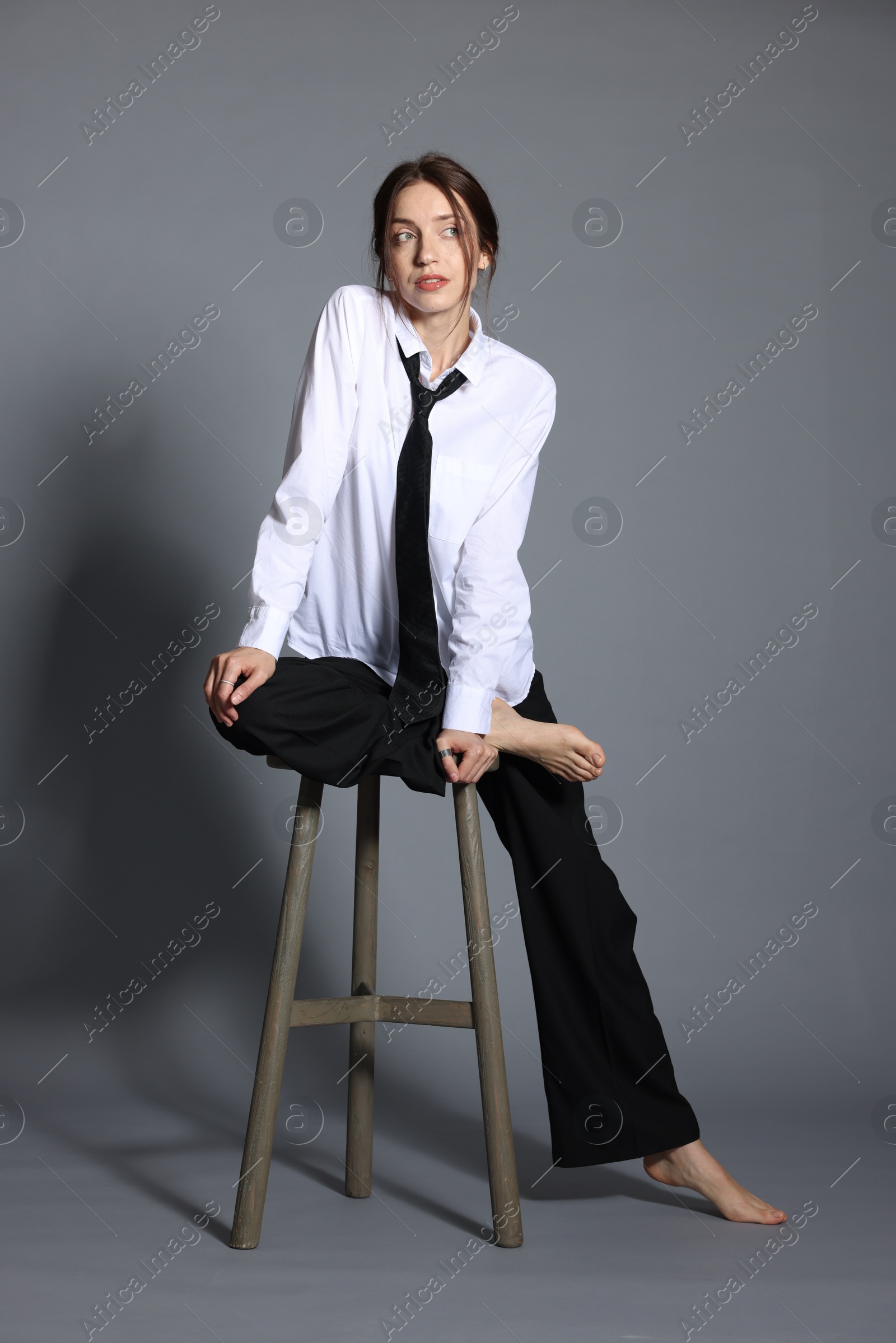 Beautiful woman in stylish outfit sitting on chair against light grey background Photo of Beautiful woman in stylish outfit sitting on chair against light grey background