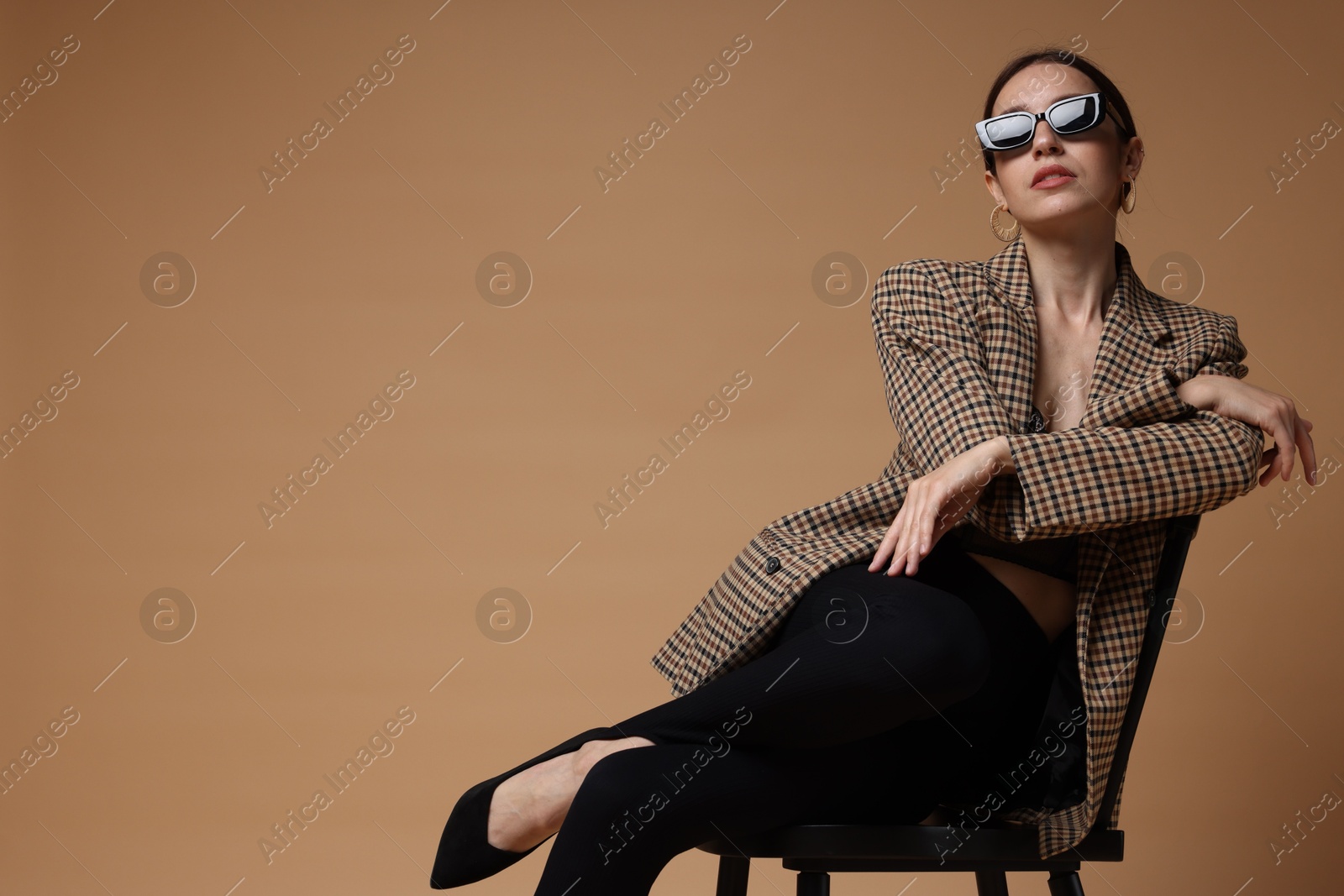 Beautiful woman in stylish outfit sitting on chair against beige background, space for text Photo of Beautiful woman in stylish outfit sitting on chair against beige background, space for text
